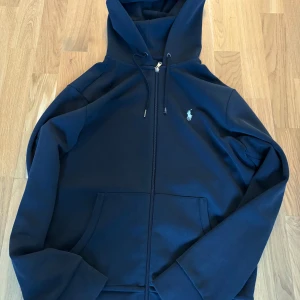Ralph lauren zip svart  - Snygg svart hoodie från Ralph Lauren med dragkedja och klassisk logga på bröstet. Tröjan har huva med snörning och stora fickor framtill. I bra skick men lite sliten på snörena, storlek s och passar som s.