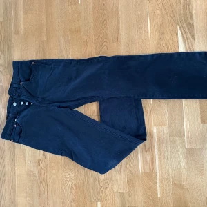 Levi's 501 svarta jeans W31 L32 - Svarta Levi's 501 jeans med klassisk rak passform och knappgylf. Jeansen har fyra fickor och är tillverkade i slitstarkt bomullstyg. Perfekta för dig som gillar en tidlös och clean look.