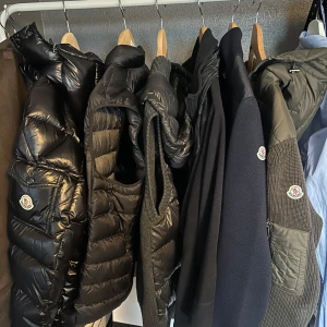 Olivgrön cardigan jacka från Moncler - Säljer en olivgrön cardigan jacka från Moncler med stickade ärmar och rygg samt quiltad, vadderad front och huva. Jackan har dragkedja och Moncler-logga på ärmen. Perfekt för dig som vill ha en snygg och bekväm lager-på-lager-look. Kvitto med mera tags bilder finns privat passar om du har S-M