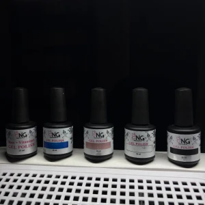 NG Gel Polish + Base - Fem flaskor NG Gel Polish + en base, 15 ml vardera. Färgerna varierar mellan rosa, blå och neutrala toner. Flaskorna har svart lock och vit etikett med blommönster. 70kr styck.
