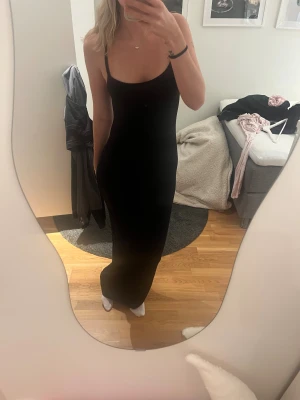 Svart långklänning med smala axelband - Säljer en svart långklänning med smala axelband och figurnära passform. Klänningen har en enkel och stilren design med rundad urringning och ärmlös siluett. Perfekt för dig som gillar minimalistisk stil och vill ha en klänning som framhäver kroppen.