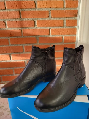 Svarta chelsea boots från Vagabond Amina - Snygga svarta chelsea boots från Vagabond i äkta skinn. Klassisk design med rund tå, låg klack och resår på sidorna för enkel påtagning. Dragkedja på insidan och diskret logga på hälen. Perfekta för dig som gillar stilrena och tidlösa skor.