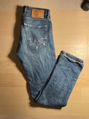 Nästan helt oanvända Replay Grover blå jeans med slitningar - Säljer ett par Replay Grover jeans i klassisk blå tvätt med snygga slitningar och detaljerade sömmar på bakfickorna. Jeansen har rak passform, normal midja och är tillverkade i robust denim. Perfekt för dig som gillar en avslappnad och cool stil.