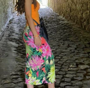 Blommig långkjol från H&M, strl 36 - Färgstark långkjol från H&M med tropiskt blommigt mönster i rosa, gul, grön, orange och svart. Kjolen har en rak passform och är tillverkad i ett lätt och luftigt material. Snygg att styla med crop top eller linne.