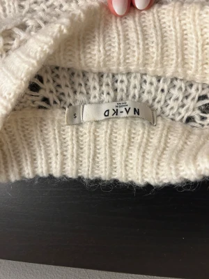 Vit stickad tröja från NA-KD - Säljer en vit stickad tröja från NA-KD i storlek S. Tröjan har ett snyggt hålmönster framtill och på ärmarna, samt ribbade muddar vid hals, ärmslut och nederkant. Perfekt för dig som gillar mysiga och trendiga plagg med lite extra detaljer.