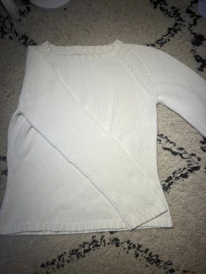 Vit stickad tröja med rund hals - Säljer en enkel och stilren vit stickad tröja med rundad hals och långa ärmar. Tröjan har ribbade muddar vid hals, ärmslut och nederkant. Perfekt för dig som gillar en clean look och vill ha något mjukt och bekvämt.