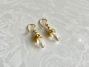 Glittriga örhängen med kristall och guld - Snygga örhängen med droppformad, facetterad kristallpärla och guldfärgade detaljer. De har en liten vit pärla och en glittrig ring med små stenar som ger extra bling. Perfekta för dig som gillar unika och eleganta accessoarer.