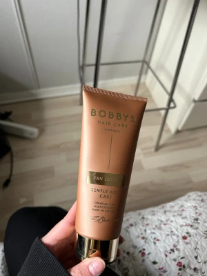 Bobbys Tan Lotion - Bobbys Tan Lotion är en brunaktig body lotion som ger huden en jämn, solkysst ton. Tuben är kopparfärgad med gulddetaljer och rymmer en gradvis brun-utan-sol-effekt. Innehåller återfuktande ingredienser och absorberas snabbt utan att kladda.