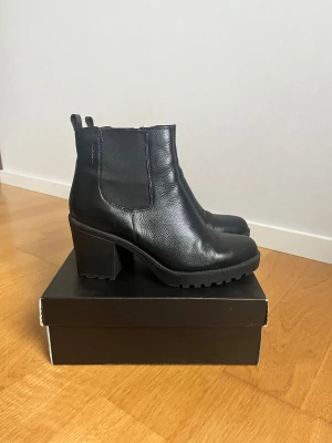 Svarta chelsea boots med klack - Snygga svarta chelsea boots från Vagabond i skinn med grov platt sula och stabil klack. Bootsens elastiska paneler på sidorna och dragkedja gör dem enkla att ta på. Rund tå och klassisk siluett som passar till många stilar.