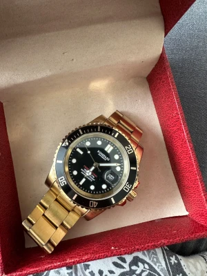 Guldfärgad Kompass klocka med svart urtavla - Säljer en stilren Kompass klocka med guldfärgat metallarmband och svart urtavla. Som ny