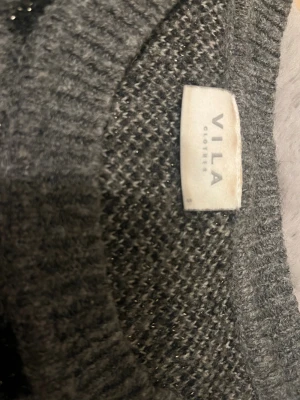 Grå leopardmönstrad stickad tröja VILA - Snygg grå stickad tröja från VILA i storlek S med leopardmönster i svart och vitt. Tröjan har rund halsringning och långa ärmar. Materialet är mjukt och har en lätt glittrig effekt som gör den extra cool. Perfekt för dig som gillar djurmönster och vill sticka ut.