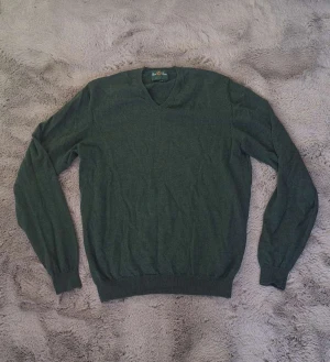 Grön merinotröja från Alan Paine stl XL - Snygg mörkgrön stickad tröja från Alan Paine i ren merinoull. V-ringad modell med långa ärmar och ribbade muddar vid ärmslut och nederkant. Nypris 1800 kr, helt oanvänd. Använd max 5 gånger. 
