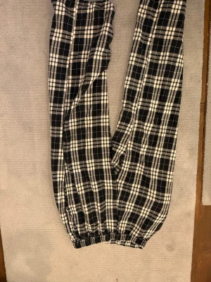 Svarta och vita rutiga byxor Madlady - Rutiga byxor från Madlady i svart och vitt med elastisk midja och benslut. Tillverkade i mjuk bomull, perfekta för chill dagar. Mönstret är klassiskt rutig och byxorna har en loose passform som ger en avslappnad vibe.