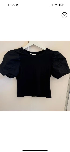 Svart puffärm topp  - Svart topp från H&M i storlek XS med puffiga korta ärmar och rund halsringning. Kroppsdelen är i mjuk bomull medan ärmarna har en lite styvare känsla som ger extra volym. Enkel och stilren design som ändå sticker ut med sina coola ärmar.