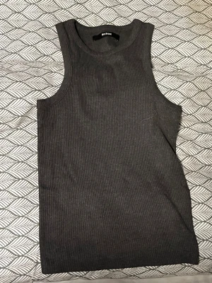 Mörkgrå ribbad linnetopp från Bik Bok - Säljer en stilren mörkgrå linnetopp från Bik Bok. Toppen är ribbad och har en ärmlös design med rund halsringning. Perfekt för dig som gillar enkla och snygga basplagg. Materialet är mjukt och stretchigt för en bekväm passform.