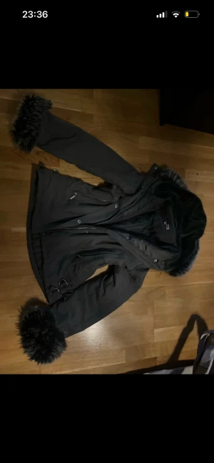 Mörk grön jacka  - Snygg mörk grön jacka med fluffiga pälsdetaljer på huva och ärmslut. 