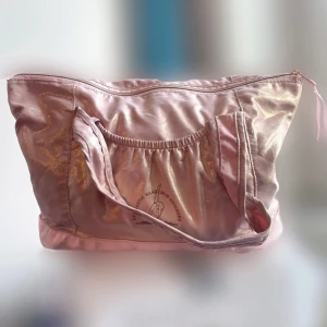 Glittrig rosa väska - Stor glittrig rosa väska med dragkedja och dubbla handtag. Framsidan har en elastisk ficka med tryck. Perfekt för att bära med sig allt man behöver. 