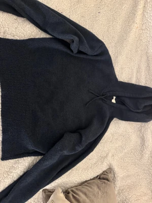 Mörkblå stickad hoodie från Gina Tricot - Mysig mörkblå hoodie från Gina Tricot i stickat material. Tröjan har huva med snörning och långa ärmar, samt bred ribbad kant nedtill. Perfekt för dig som gillar chill och enkel stil.