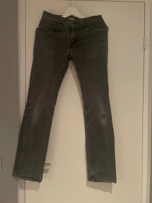 Levi's 511 Slim grå jeans - Snygga grå Levi's 511 Slim jeans med klassisk femficksdesign och diskret slitning. Jeansen har en slim passform och raka ben, med detaljer som Levi's patch och röd etikett bak. Perfekt för dig som gillar en stilren look med edge.