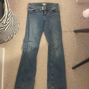 Blå bootcut jeans från Gina Tricot - Snygga blå jeans från Gina Tricot i storlek 164. Modellen har bootcut-ben, klassisk femficksdesign och dubbla knappar framtill. Jeansen är tillverkade i jeansmaterial med en cool tvättad look och passar perfekt till en trendig streetstyle.