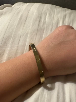 Guldfärgat armband med stjärnor - Snyggt guldfärgat armband i metall med ingraverade stjärnor runt om. Stilren och enkel design som passar perfekt för dig som gillar detaljer med lite extra edge. Armbandet är stelt och har en blank finish.