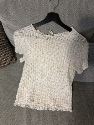 Natur vit T-shirt från Aware - Säljer en söt T-shirt från Nelly  med korta ärmar och vacker spets över hela toppen. T shortsen  har rund halsringning och fina vågiga kanter vid ärmslut och nederkant. Perfekt för dig som gillar romantisk och feminin stil!