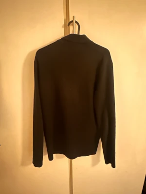 Svart pikétröja från Filippa K - Snygg svart pikétröja från Filippa K med klassisk krage och knappar framtill. Tröjan har lång ärm och är gjord i mjukt material som känns skönt mot huden. Perfekt för dig som gillar stilrena och enkla plagg med en modern touch.