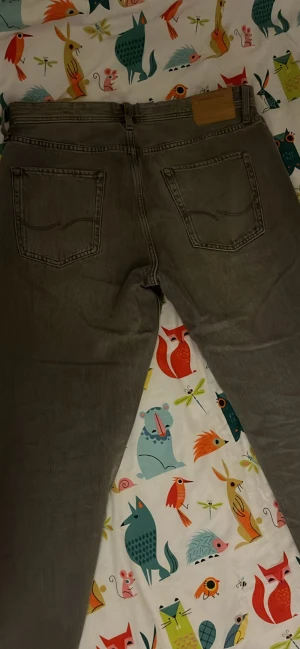 Grå relaxed jeans från Jack & Jones - Säljer ett par gråa jeans från Jack & Jones, modell Relaxed/Chris. De har en avslappnad passform med raka ben och klassiska fem fickor. Jeansen är tillverkade i slitstark denim och har snygga detaljer som metallknappar och bälteshällor.