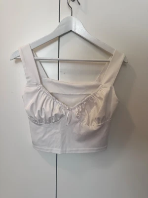 Vit croppad linnetopp med snörning - Säljer en fräsch vit croppad linnetopp med breda axelband och snygg snörning framtill. Toppen har en lätt rynkad detalj vid bysten och är tillverkad i mjukt bomullsmaterial. Perfekt för dig som gillar stilrena och trendiga plagg.