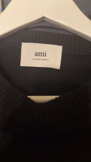 Svart stickad tröja från Ami Paris  - Svart stickad tröja från Ami Paris med rund hals och ribbade muddar. På bröstet finns ett stort rött hjärta med bokstaven A, vilket ger en unik och trendig look. Perfekt för dig som gillar stilrena detaljer och vill sticka ut. (Andvänd 1 gång)