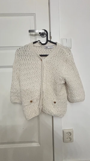 Beige stickad kofta från Zara - beige stickad kofta från Zara i storlek S. Koftan har ett grovt virkat mönster, trekvartsärmar och snygga guldfärgade knappar framtill samt på fickorna