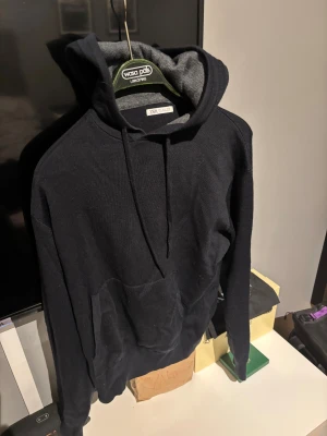 Svart hoodie från Zara i storlek L - Svart hoodie från Zara i storlek L med klassisk huva och snörning. Tröjan har en stor magficka och är tillverkad i ett mjukt stickat material. Sitter mer som M