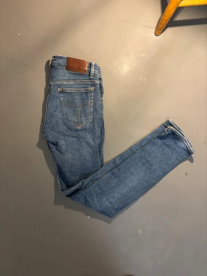 Slim jeans från Tiger of Sweden, blå - Snygga blå jeans från Tiger of Sweden i slim fit-modell. Klassisk femficksdesign med orangea sömmar och silverfärgad knapp. Jeansen är tillverkade i bomull och har en smal passform som sitter snyggt längs benen.
