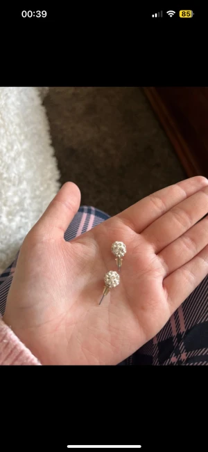 Glittriga silverfärgade örhängen - Säljer ett par snygga örhängen i silverfärg med rund form och glittriga detaljer. De är små och diskreta men ändå riktigt blingiga, perfekta om du vill ha något som syns lite extra. Passar dig som gillar stilrena accessoarer med lite sparkle.