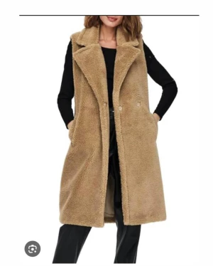 Teddyväst, ONLY - Säljer en lång, snygg och mysig beige pälsväst från ONLY. Västen är varm med två fickor framtill och stängs med knappar. Materialet är fluffigt och ger en cool teddy-look. Perfekt att slänga över en hoodie eller tröja för extra värme och stil. Västen är i väldigt gott skick nästan ny! Storlek S 🌸