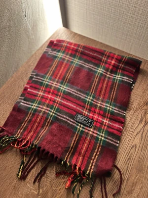 Rutig ullhalsduk från Burberrys - Klassisk rutig halsduk från Burberrys i 100% ull. Halsduken har fransar i ändarna och den ikoniska Burberrys-etiketten. Perfekt accessoar för att lyfta din outfit. Anledningen att de stör ”burberrys” är för att de är en äldre modell.