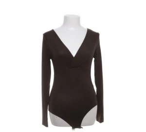 Brun ribbad v-ringad body från H&M - Snygg brun body från H&M med ribbad struktur och djup v-ringning. Långärmad modell som sitter tight och har omlott-detalj vid bysten. Perfekt att styla med jeans eller kjol för en trendig look.