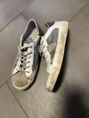 Grå Philippe Model sneakers - Snygga sneakers från Philippe Model i grått och vitt med text på snörningen. Skorna har rund tå, platt sula och detaljer i mocka och skinn. Perfekt för dig som gillar en urban och avslappnad stil.