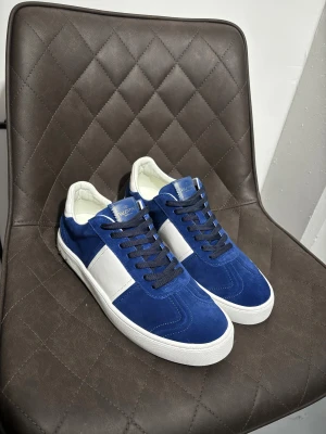 Valentino Garavani blå sneakers - Snygga sneakers från Valentino Garavani i blå mocka och vitt skinn. De har svarta snören, rund tå och platt sula med coolt mönster undertill. Baksidan är dekorerad med silverfärgade nitar för extra edge. Perfekt för dig som gillar exklusiva och stilrena sneakers. Nypris:7000 Mitt pris:4000