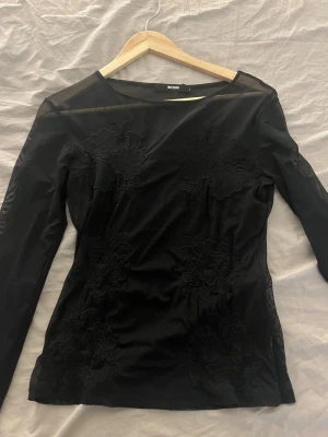 Svart mesh blus med blommor från Bik Bok - Säljer en svart mesh blus från Bik Bok i storlek L. Blusen har lång ärm och är genomskinlig med stora broderade blommor framtill. Den har en rund halsringning och är figurnära i passformen. Perfekt för dig som gillar detaljer och vill sticka ut. Passar XS-L
