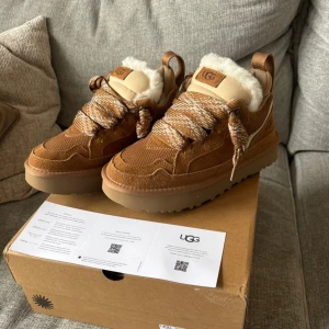 UGG Lowmel  - Säljer ett par snygga UGG Lowmel i brun mocka med fluffig päls på insidan. Skorna har grova snören i beige och vitt, tillkommer ett par extra. UGG-logga på sidan och tungans etikett. Skolåda tillkommer. Använda en gång då de va för små. Skriv om du har några funderingar! 😊