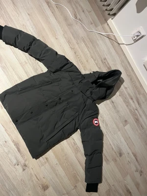 Svart dunjacka Canada Goose XS - Säljer en svart dunjacka från Canada Goose i storlek XS. Jackan har huva, långa ärmar med muddar, flera fickor och den klassiska röda Canada Goose-loggan på ärmen. Perfekt för kalla dagar och har en clean, stilren look.