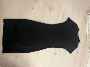 Svart ribbad kortklänning - Svart kortklänning med ribbad struktur och rund hals. Klänningen har korta ärmar och en figurnära passform som framhäver siluetten. Perfekt för dig som gillar enkel och stilren design.