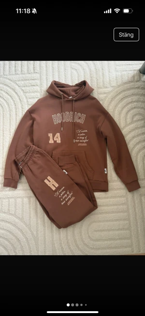 Brun hoodie från Hoodrich med tryck - Säljer en brun hoodie från Hoodrich med stort tryck på bröstet, siffran 14 och textdetaljer. Hoodien har huva med snörning, magficka och ribbade muddar. Materialet är mjuk bomull och passformen är normal. Perfekt för chill dagar och streetwear vibes. Storlek xs