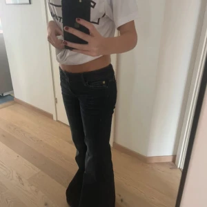 Mörkblå bootcut jeans från weekday - Säljer ett par mörkblå weekday jeans med bootcut passform och låg midja. Jeansen har klassiska fem fickor, guldfärgade detaljer vid knappar och är tillverkade i jeansmaterial. Snyggt slitna och perfekta för en cool och avslappnad stil.