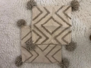 Två kuddfodral  - Två stycken söta kuddfodral med mönster fram till och små tofsar på varje hörn, i beige kulör🩷