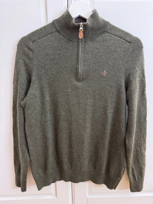 Olivgrön tröja från Morris - Snygg olivgrön tröja från Morris. Tröjan har half zip med läderdetalj på dragkedjan, ribbad krage och muddar samt ett broderat emblem på bröstet. Den är tvättad en gång och krympte efter tvätten. Tröjan har storlek L, men passar bäst som M 