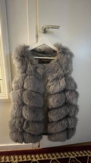 Grå pälsväst från RuiXiangTe - Fluffig och lyxig grå pälsväst från RuiXiangTe. Västen har en voluminös look med breda, horisontella sektioner och är ärmlös. Perfekt för att ge din outfit en extra touch av stil och värme under kyliga dagar. Den använd inte längre därför tänkte jag att sälja den för 600 priset kan diskuteras!