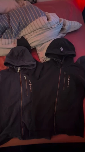 Svart och marinblå Sail Racing hoodie - Två hoodies från Sail Racing, en i svart och en i marinblå. Båda har huva, dragkedja framtill och en bröstficka med zip. Snygg logga på bröstet och på huvan. Perfekt för chill dagar och streetwear. Säljes separat eller tillsammans. 450:- för båda 250:- för en 