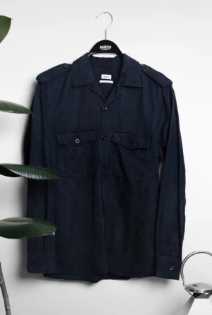 Mörkblå overshirt från Filippa K - Snygg mörkblå overshirt från Filippa K med klassisk krage, axelklaffar och två bröstfickor med knappar. Skjortan har lång ärm och relaxed fit, perfekt för en chill och stilren look. Tillverkad i mjuk bomull som känns skön mot huden.